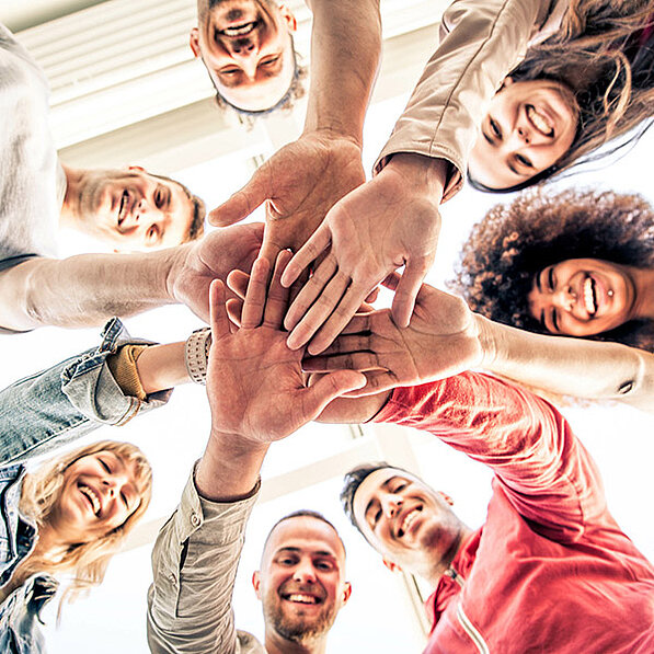 Diverse Gruppe streckt Hände zum Teamwork in die Mitte