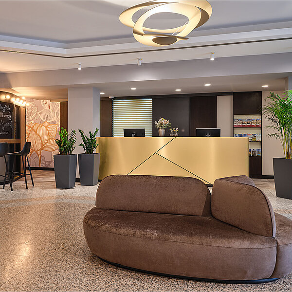 Moderne Hotellobby mit braunem Sofa und goldenem Empfangstresen