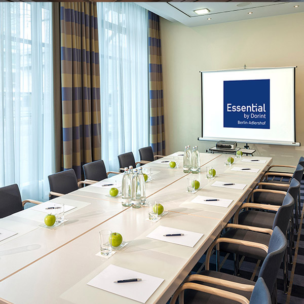 Heller Konferenzraum mit langem Tisch, schwarzen Stühlen und Essential by Dorint Logo an der Wand