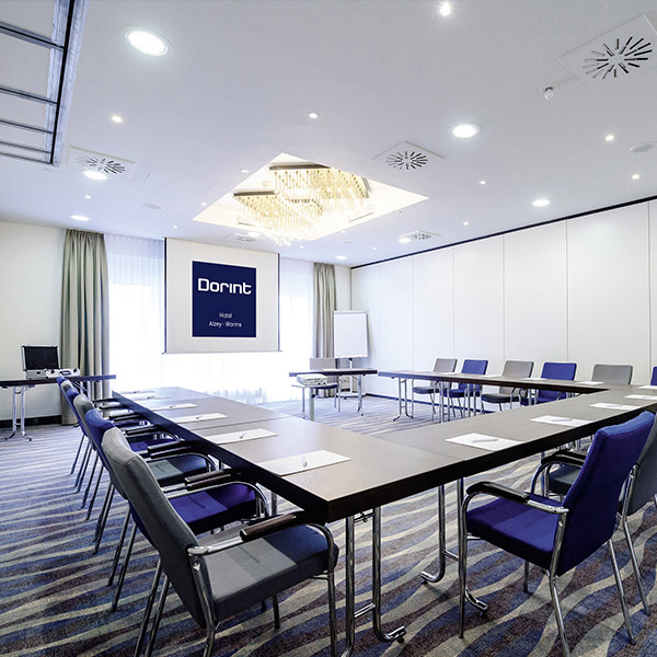 Moderner Tagungsraum mit U-förmiger Tischstellung, blauen Stühlen und eleganter Deckenbeleuchtung