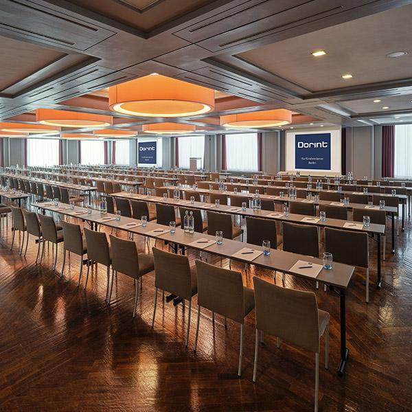 Großer Konferenzsaal mit Reihenbestuhlung, orangefarbenen Deckenleuchten und Dorint Branding