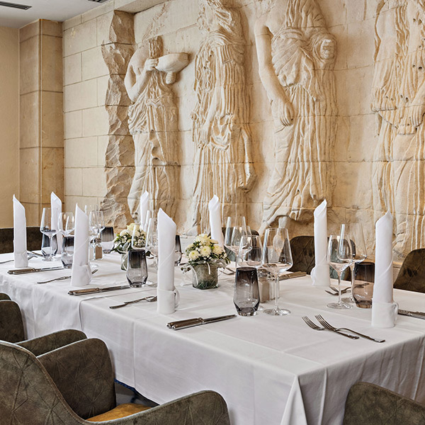 Eleganter Restaurantbereich mit weißen Tischdecken, Kerzen und antiker Steinrelief-Wandgestaltung