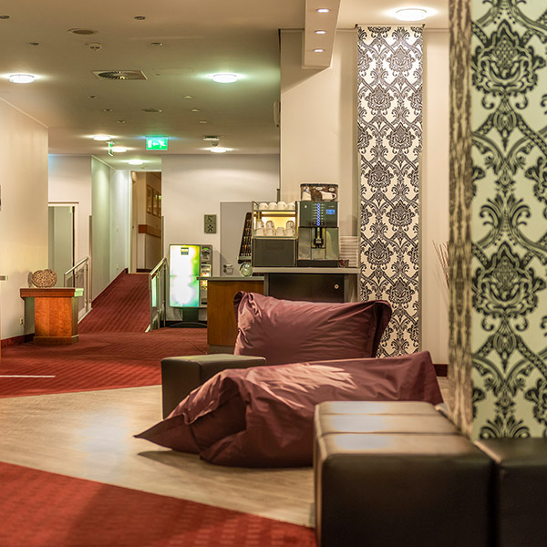 Moderne Hotellobby mit gemusterten Tapeten, Sitzecke und Kaffeemaschine im Hintergrund