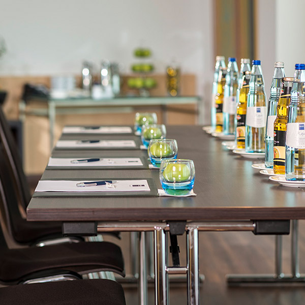 Detailaufnahme eines gedeckten Konferenztisches mit Wasserflaschen und grünen Äpfeln