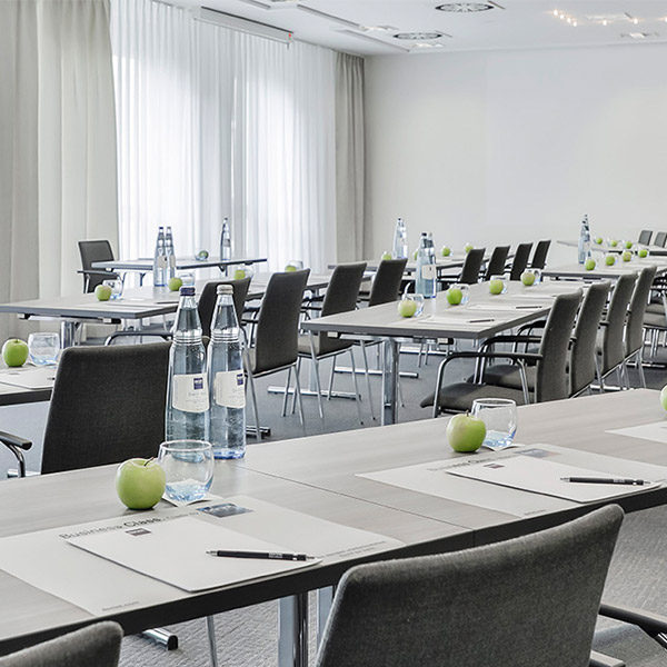 Heller Konferenzraum mit grauen Stühlen, weißen Vorhängen und grünen Äpfeln auf den Tischen