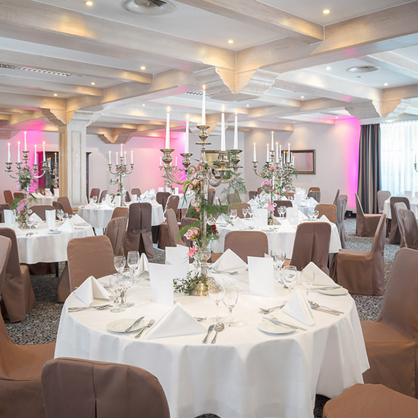 Eleganter Bankettsaal mit runden Tischen, weißen Tischdecken und rosa Beleuchtung