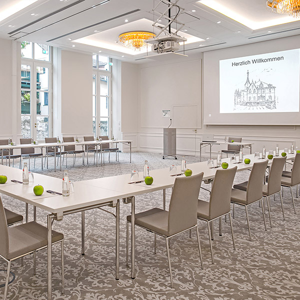 Moderner Konferenzraum mit U-förmiger Tischanordnung, Stühlen, Wasserflaschen und grünen Äpfeln