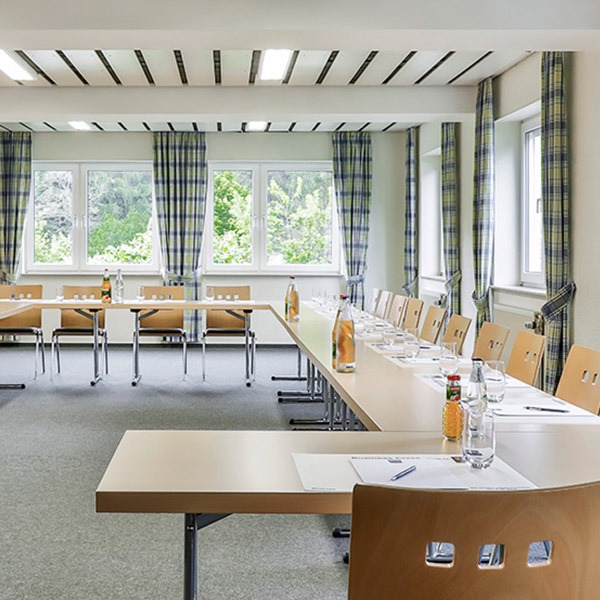 Ein Konferenzraum mit U-förmiger Tischanordnung, Stühlen, Wasserflaschen und Schreibmaterialien