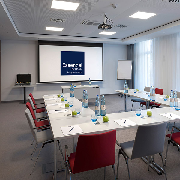 Konferenzraum mit Tischen, Stühlen, Wasserflaschen und Äpfeln vor einer Leinwand