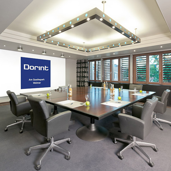 Moderner Konferenzraum mit großem Tisch, Stühlen und Dorint-Logo an der Wand projiziert