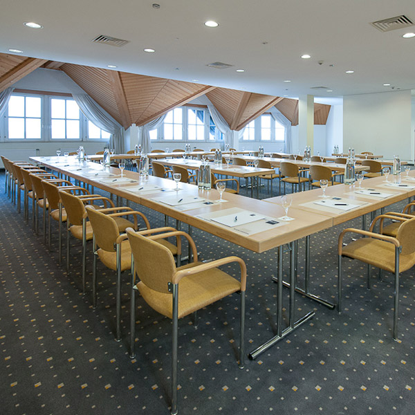 Konferenzraum mit langen Tischen, Stühlen und Schreibmaterialien