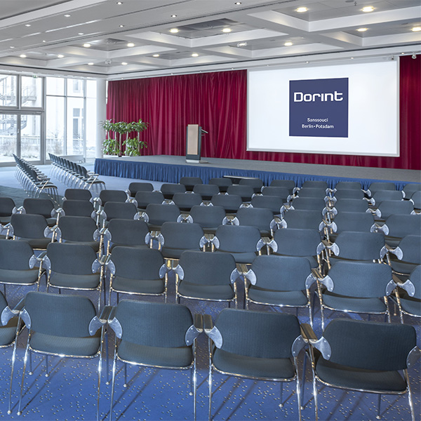 Moderner Konferenzraum mit Stuhlreihen, einer Bühne mit rotem Vorhang und Leinwand mit Dorint Logo