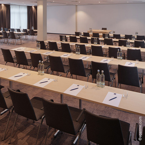 Konferenzraum mit Reihen von Tischen und Stühlen, Wasserflaschen und Schreibmaterialien
