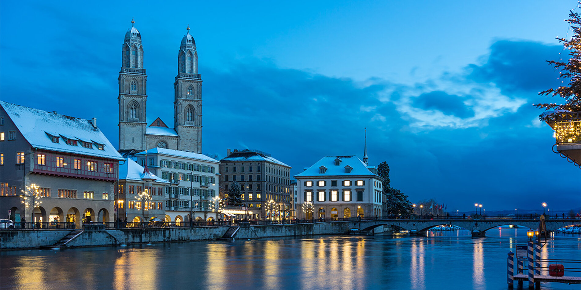 Grossmünster und Limmat in Zürich bei Dämmerung mit Schnee und Weihnachtsbaum