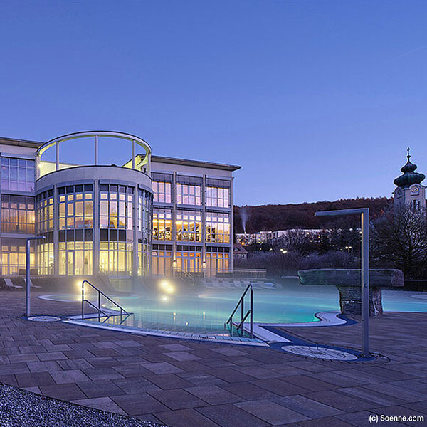Modernes Wellnesshotel mit Außenpool und beleuchteter Glasfassade in der Abenddämmerung